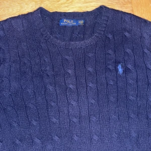 Mörkblå stickad tröja från Polo Ralph Lauren - Säljer en snygg mörkblå stickad tröja från Polo Ralph Lauren. Den har ett klassiskt flätmönster och den ikoniska loggan broderad på bröstet. Perfekt för kyliga dagar och passar både till vardags och lite finare tillfällen. Tröjan är i mycket bra skick och redo för en ny ägare! Ny pris 2000kr