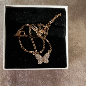 Guldhalsband med fjärilshänge - Säljer ett superfint guldhalsband med ett glittrigt fjärilshänge. Perfekt för att lägga till lite bling till din outfit! Kedjan är tunn och elegant, och fjärilen är täckt med små gnistrande stenar. Passar både till vardags och fest. 🦋✨