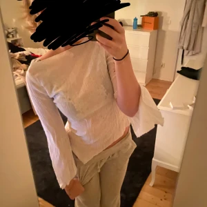 Vit långärmad topp - Säljer en superfin vit topp med långa ärmar och volangdetaljer vid ärmsluten. Toppen har en tight passform och är perfekt för både vardag och fest. Den är i mycket bra skick och gjord av ett mjukt material som känns skönt mot huden.