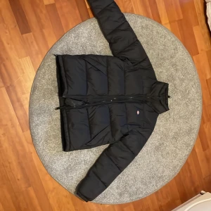 Svart pufferjacka från Dickies - Säljer en svart pufferjacka från Dickies i äkta dun i storlek smal. Jackan är perfekt för kalla dagar med sin quiltade design och dragkedja framtill. Den har en klassisk stil och är riktigt varm och skön. Passar perfekt för vintern!