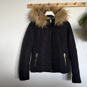 Svart pufferjacka från ONLY - Säljer en snygg svart pufferjacka från ONLY i storlek S. Jackan har en mysig fuskpäls på huvan och dragkedja framtill. Perfekt för kalla vinterdagar med sin quiltade design och långa ärmar. Den är gjord av polyester vilket gör den både varm och lätt att bära. Två praktiska fickor med dragkedja finns på framsidan.