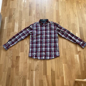 Rutig skjorta från Berkeley - Säljer en snygg rutig skjorta från Berkeley i en casual slim fit. Skjortan har ett klassiskt rutmönster i rött, blått och vitt med knappar framtill. Perfekt för både vardag och fest!
