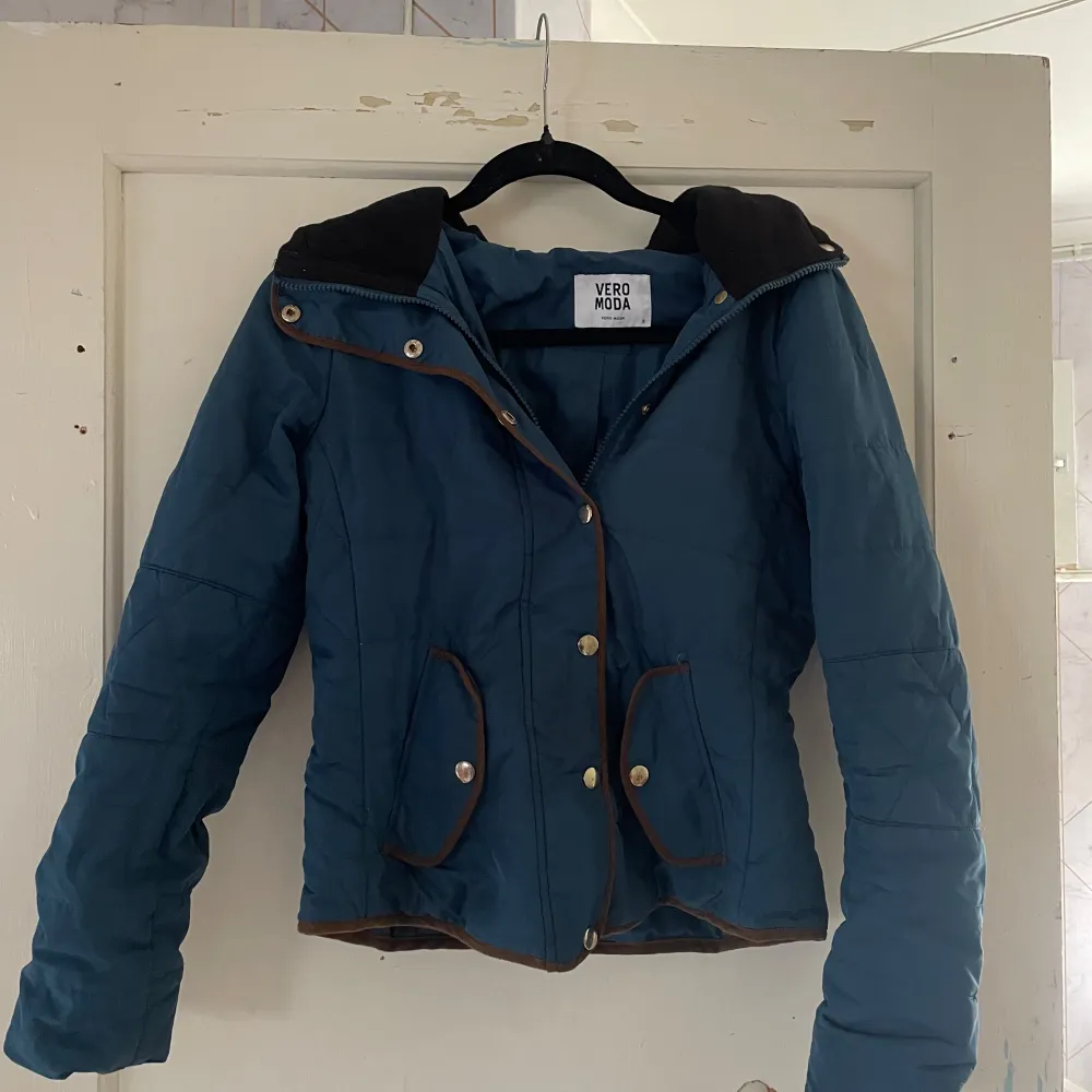 Säljer en snygg blå jacka från Vero Moda. Den har en dragkedja och knappar framtill, samt praktiska fickor med knappdetaljer. Jackan är perfekt för höst och vår, med en stilren design och bekväm passform.. Takit.