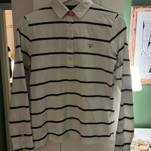 GANT långärmad piké - Denna stiliga piké är använd ett fåtal gånger och i mycket bra skick. Den är vit med svarta ränder. Den är liten i storleken men passar en XS. Passa på!