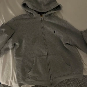 Polo ralph lauren ziphoddie grå - Jag säljer min grå ziphoddie för att den är för liten, strl 14-16 S, finns en liten fläck på tröjan men det märkar man nog inte, bara skriva om du har några frågor!