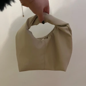 Beige handväska - Säljer en superfin beige handväska i syntetmaterial. Den har en enkel och stilren design med en praktisk öppning och en liten knappstängning. Fint skick! Osäker på vilket märke det är. Säljer för 175 kronor💞💞
