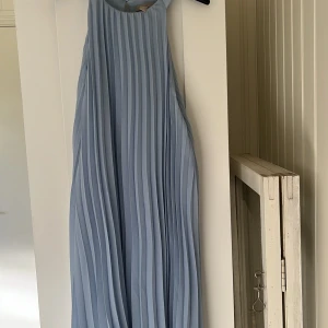 Plisserad klänning - En blå plisserad klänning. går precis över knäna på mig som är 170 cm. Katt finns i hemmet