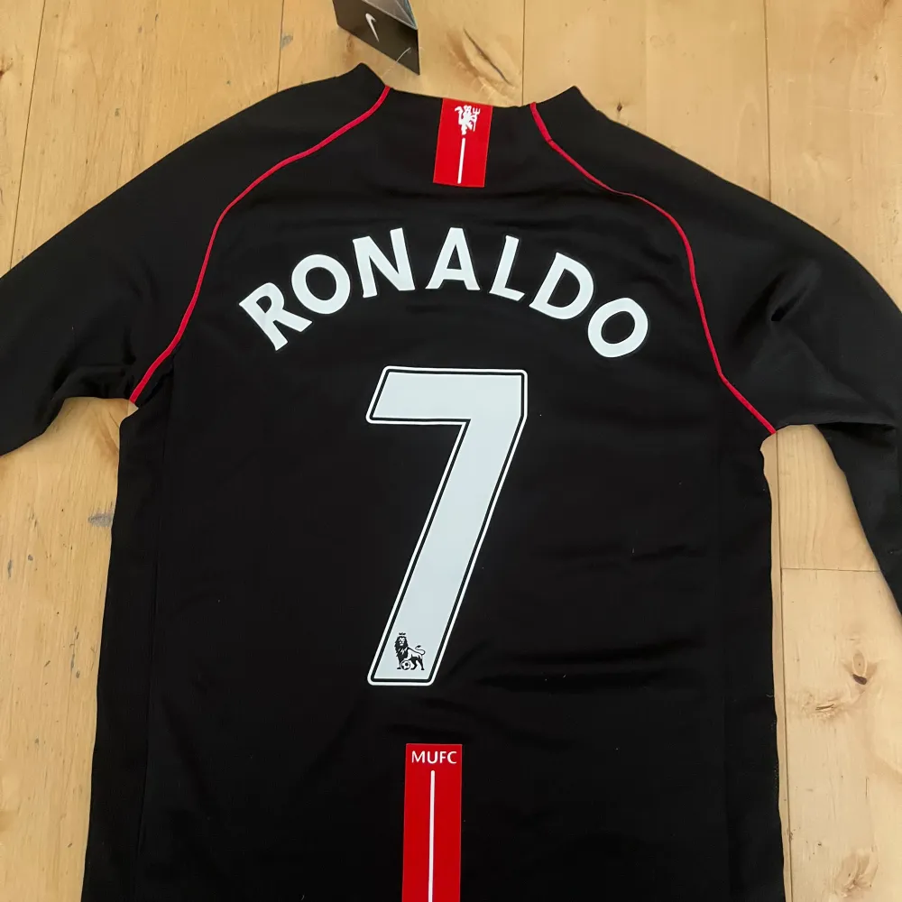 Säljer en svart Manchester United fotbollströja från Nike.Tröjan har långa ärmar och är i nyskick har endast provat en gång. På baksidan står det 'Ronaldo' med nummer 7. För liten på mig. Sportswear.