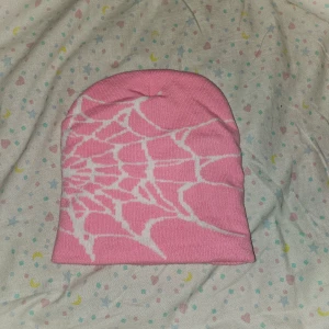 Rosa mössa - En rosa mössa med ett vitt spindelnätsmönster. Mössan är ny.