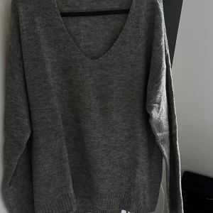 Grå stickad tröja - Säljer en mysig grå stickad tröja med v-ringning. Perfekt för kyliga dagar och passar till allt! Tröjan har långa ärmar och en avslappnad passform. Superbekväm och stilren!