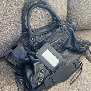 Balenciaga city väska  - Säljer min fina balenciaga väska i svart läder med guld detaljer! Väskan är i bra skick med tecken på användning, framförallt på bandet, spegeln och handtaget. Väskan är köpt på vestaire collective. 
