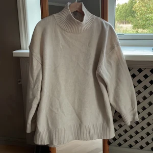 STICKAD TRÖJA - Ljus beige stickad tröja från H&M. Halvpolitisk med en liten slits i nacken, längre modell så den går ner strax under rumpan, Höga slits på båda sidor. 