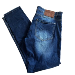 Blå jeans från Dsquared2 - Säljer ett par snygga blå jeans från Dsquared2. De har en cool distressed look med slitningar och färgstänk som ger en unik stil. Perfekta för en casual outfit med en t-shirt eller hoodie. Jeansen har en klassisk femficksdesign och en bekväm passform