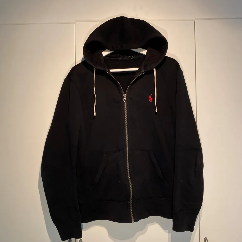 Polo Ralph Lauren Zip-Hoodie i svart med röd häst. Fint skick utan skador. Storlek M. Unisex. Nypris 1900kr. Stilsäker som går att både dressa upp & ner. Grymt bra basplagg i garderoben. Funkar året runt. Pris kan diskuteras. Hör av dig i DM! . Hoodies.