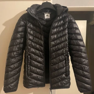 Dunjacka med huva - Säljer en snygg svart dunjacka från McKinley. Jackan är perfekt för kalla dagar med sin quiltade design och huva som håller dig varm. Den har en dragkedja framtill och är långärmad. Passar perfekt för både höst och vinter! Använd, hål inuti fickan!