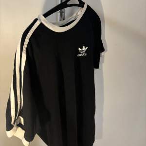 Säljer en snygg svart och vit tröja från Adidas. Den har de klassiska tre ränderna på ärmarna och Adidas-loggan på bröstet. Perfekt för en sportig look eller bara för att chilla i. Nypris: 299kr