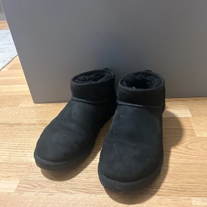 Svarta boots från UGG - Säljer ett par svarta boots från UGG i mocka med mjukt foder. Perfekta för kyliga dagar med en stilren design och bekväm passform.