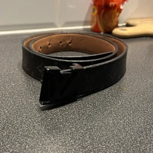 Lv bälte, vill byta mot burberry bälte - Snyggt svart bälte från Louis Vuitton med ett stilrent monogramspänne. Bältet har en klassisk design med diskret mönster och är perfekt för att lyfta vilken outfit som helst.