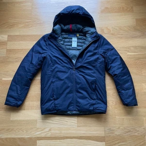 Polo Ralph Lauren Jacka - Denna marinblå Polo Ralph Lauren-jacka är i utmärkt skick, som ny, med originaletiketterna noggrant bifogade. Den har bara provats på ett fåtal gånger, så den är perfekt för dig som söker både stil och funktionalitet. Den är vatten- och vindavvisande. Den är lätt och packbar. Jag skickar inom 24 timmar efter köp.  Mått: Längd (axlar till midja): 66CM Bredd: (axel till axel): 46CM Ärmlängd (axlar till handled): 61CM