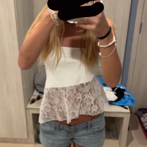 Vit ärmlös topp med spetsdetaljer - Säljer en söt vit ärmlös topp med spetsdetaljer nedtill. Toppen har en luftig passform och är perfekt för varma dagar. Den är enkel att matcha med jeans eller kjol för en avslappnad look.