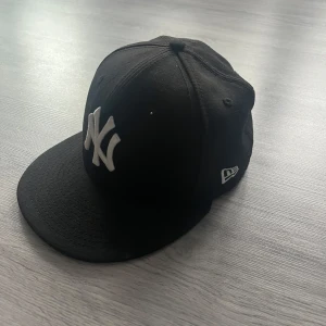 Svart keps från New Era - Snygg svart keps från New Era med klassisk vit broderad logga framtill. Kepsen är en 59FIFTY-modell med en platt skärm och stängd baksida. Perfekt för en stilren look. Fraktan inom 12 timmar pris kan diskuteras 📦🚚✅