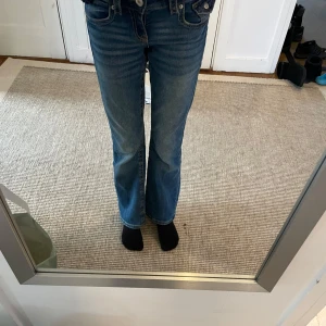 Blå bootcut jeans - Snygga blå bootcut jeans med klassisk femficksdesign och knappgylf. Perfekta för en avslappnad stil med en touch av retro. De har en bekväm passform och är tillverkade i slitstarkt denim.