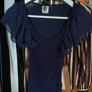 Mörkblå topp från ICHI - Säljer en elegant mörkblå topp från ICHI med volangdetaljer på ärmarna. har en rund halsringning och är perfekt för en stilren look. Materialet är lätt och luftigt, vilket gör den bekväm att bära.