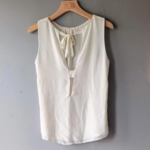 blus med rosett rosett  - Snygg vit blus med knytning i ryggen och dekorativ kant vid halsen. Perfekt för en stilren look.