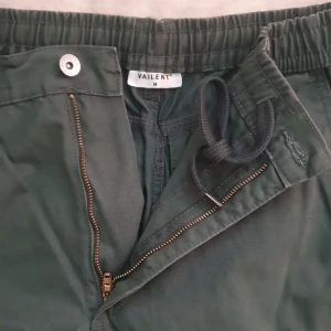 Gröna cargobyxor från Vaillent - Snygga gröna cargobyxor från Vaillent med elastisk midja och snörning. Byxorna har praktiska fickor på sidorna och en dragkedja framtill. Perfekta för en avslappnad stil.