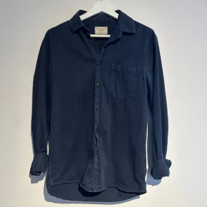 Mörkblå skjorta från Nudie Jeans Co - Snygg mörkblå skjorta från Nudie Jeans Co i herrstorlek XS. Skjortan har långa ärmar och en klassisk krage med knappar framtill. Perfekt för en stilren look.