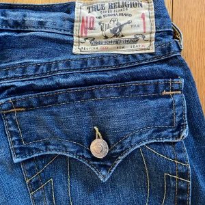Blå jeans från True Religion - Snygga loose jeans från True Religion med unika detaljer som stjärnmönster av nitar på framsidan. Klassisk femficksdesign och knappar med logotyp. Perfekta för dig som vill ha en stilren men ändå iögonfallande look. Pris kan diskuteras:)