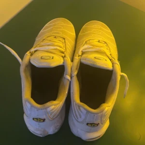 Vita sneakers från Nike - Snygga vita sneakers från Nike med TN-logga på hälen. Skorna har en sportig design med snörning och synliga luftkuddar i sulan för extra komfort. Perfekta för en casual look.