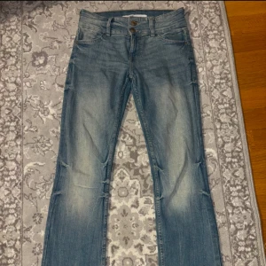 Blå bootcut jeans från Bershka - Snygga blå bootcut jeans från Bershka med dubbla knappar i midjan. De har en klassisk femficksdesign och en lätt tvättad look. Perfekta för en avslappnad stil.