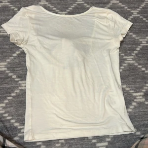 Vit topp med rosett från 157 - Säljer en söt vit topp från 157 i storlek XS. Toppen har korta ärmar och en v-ringning med en stor dekorativ rosett baktill. Perfekt för en stilren och feminin look.