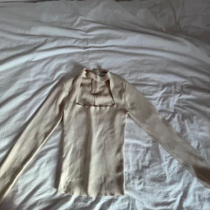 Beige långärmad topp från Zara - Säljer en stilren beige långärmad topp från Zara. Toppen har en unik design med en fyrkantig detalj framtill och en dragkedja bak. Den har spruckit lite framtill.