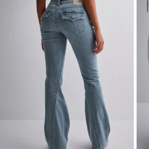 Blå bootcut jeans - Snygga blå bootcut jeans med låg och klassisk femficksdesign. Jeansen har dekorativa sömmar på bakfickorna och en knappgylf. Perfekta för en avslappnad stil.