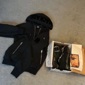Svart hoodie från Mackage paketpris med skor - Säljer en stilren svart hoodie från Mackage med dragkedjor och justerbar huva. Hoodien har långa ärmar och en snygg logga på huvan. Perfekt för en casual look. Paketpris kör jag på båda, jackan har kvitto och helt nya skorna är använda
