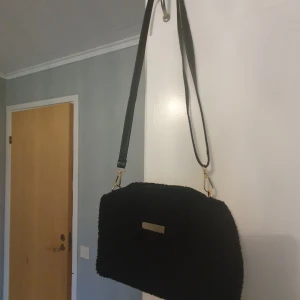Svart axelväska med gulddetaljer - Snygg svart axelväska i teddy material med guld detaljer och justerbar axelrem, som även kan tas av. Inga tecken på användning💘🤗 GE PRISFÖRSLAG