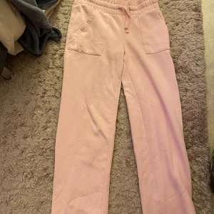 Rosa mjukisbyxor - Säljer ett par bekväma rosa mjukisbyxor med elastisk midja och snörning. Byxorna har praktiska fickor fram och bak, perfekt för en avslappnad stil. Materialet ser mjukt och skönt ut, idealiskt för mysiga dagar hemma. Köpt på Vinted, säljer då jag tyckte dom va förkorta för mig som är 170cm. Finns nån liten fläck men går säkert att få bort i tvätten