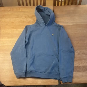 Blå lylescott hoddie - Säljer en snygg blå hoodie med ett litet emblem på bröstet. Tröjan har en klassisk känguruficka och ribbade muddar vid ärmslut och nederkant. Perfekt för en avslappnad stil. Nästan helt oanvänd. Passar s och m 