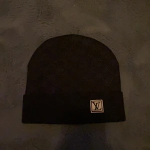 Svart mössa med logotyp - Snygg svart mössa med en stilren logotyp framtill. Perfekt för att hålla värmen under kyliga dagar. Enkel och tidlös design som passar till det mesta.