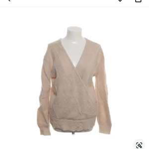 Beige omlott tröja från NA-KD - Säljer en beige omlott tröja från NA-KD i en mjuk och skön blandning av akryl, polyester, ull och mohair. Tröjan har en v-ringad design och långa ärmar, perfekt för kyligare dagar. En stilren och bekväm tröja för din garderob.