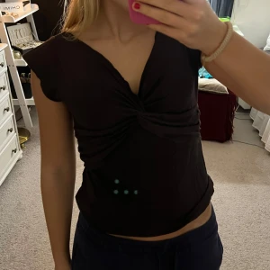 Brun topp från H&M - Snygg brun topp från H&M med en knytdetalj framtill. Toppen har korta ärmar och en v-ringad design som ger en elegant touch. Perfekt för både vardag och festliga tillfällen.