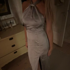 blå halterneckklänning - Elegant ljusblå halterneckklänning med öppen rygg och knytband. Klänningen har en slits framtill och är i ett glansigt material som ger en lyxig känsla. Perfekt till bal eller fest! Prislapp kvar aldrig använd! köpt för 799kr