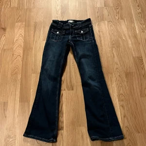 Mörkblå bootcut jeans från Gina Tricot i storlek 152 - Snygga mörkblå bootcut jeans från Gina Tricot med klassisk femficksdesign och knappar fram. Perfekta för en avslappnad stil med en touch av retro.