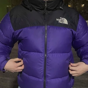 Lila och svart pufferjacka från The North Face - Säljer en snygg lila och svart The north face 700 jacka i storlek L. Perfekt inför vintern då den är riktigt varm. Skriv om ni har några frågor.