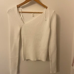 Vit ribbad tröja från H&M - Säljer en stilren vit ribbad tröja från H&M. Tröjan har en unik omlott-design med långa ärmar och en smickrande passform. Perfekt för att skapa en chic look.