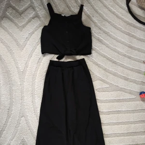 Svart ärmlös topp med knappar med tillhörande vida byxor, strl 152 - Snygg svart ärmlös topp med knappar framtill. Perfekt för en stilren look. Matchande med byxor eller för en komplett outfit.  Storlek; 152 