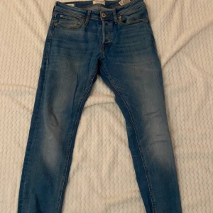 Blå jeans från Jack & Jones - Snygga blå jeans från Jack & Jones i modellen Slim Fit Tim. De har en klassisk femficksdesign och är perfekta för en stilren look. Passar bra till både vardag och mer uppklädda tillfällen.