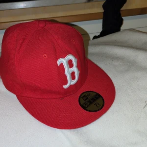 Röd keps från New Era (rödare än på bilden)  - Snygg röd keps från 90-tal New Era med ett broderat vitt 'B' på framsidan. Kepsen är en 59FIFTY-modell och har en klassisk passform. Perfekt för att ge din outfit en sportig touch.
